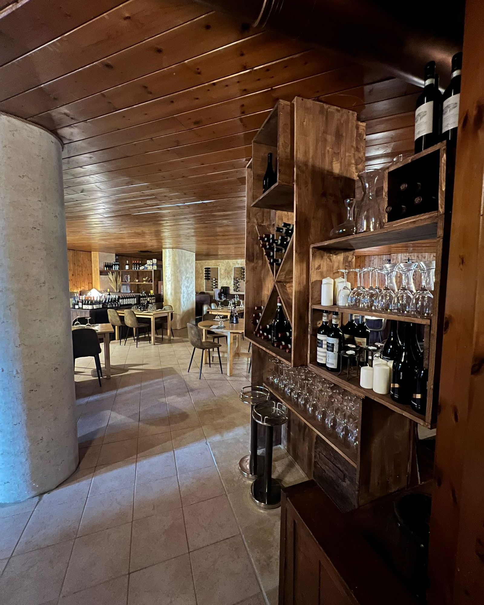 Interno del ristorante con scaffali in legno su cui sono esposti vino e bicchieri; tavoli e sedie sono visibili.