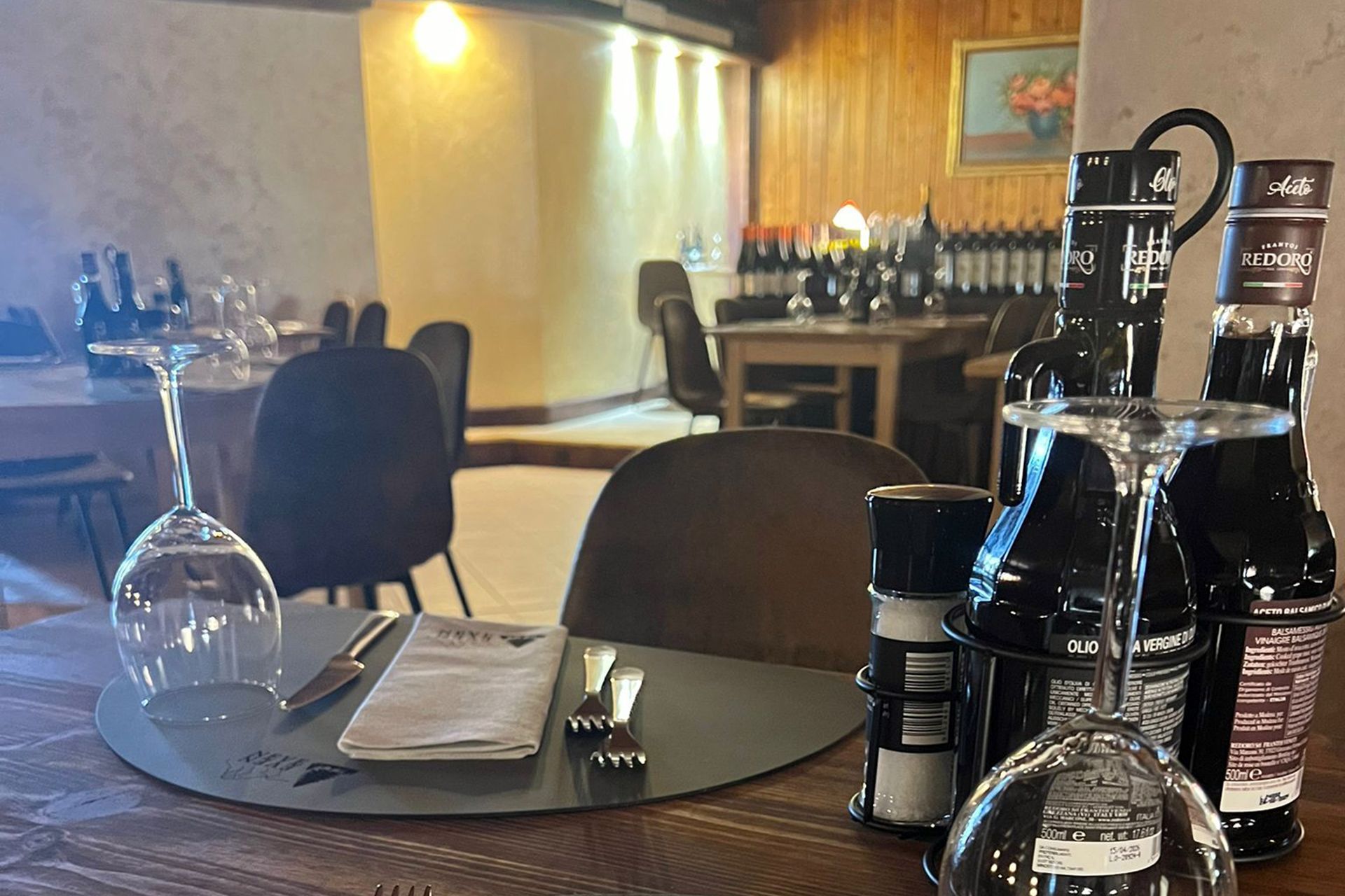 Tavolo da pranzo apparecchiato per un pasto in un ristorante; sono visibili bottiglie di vino, bicchieri e un menu.