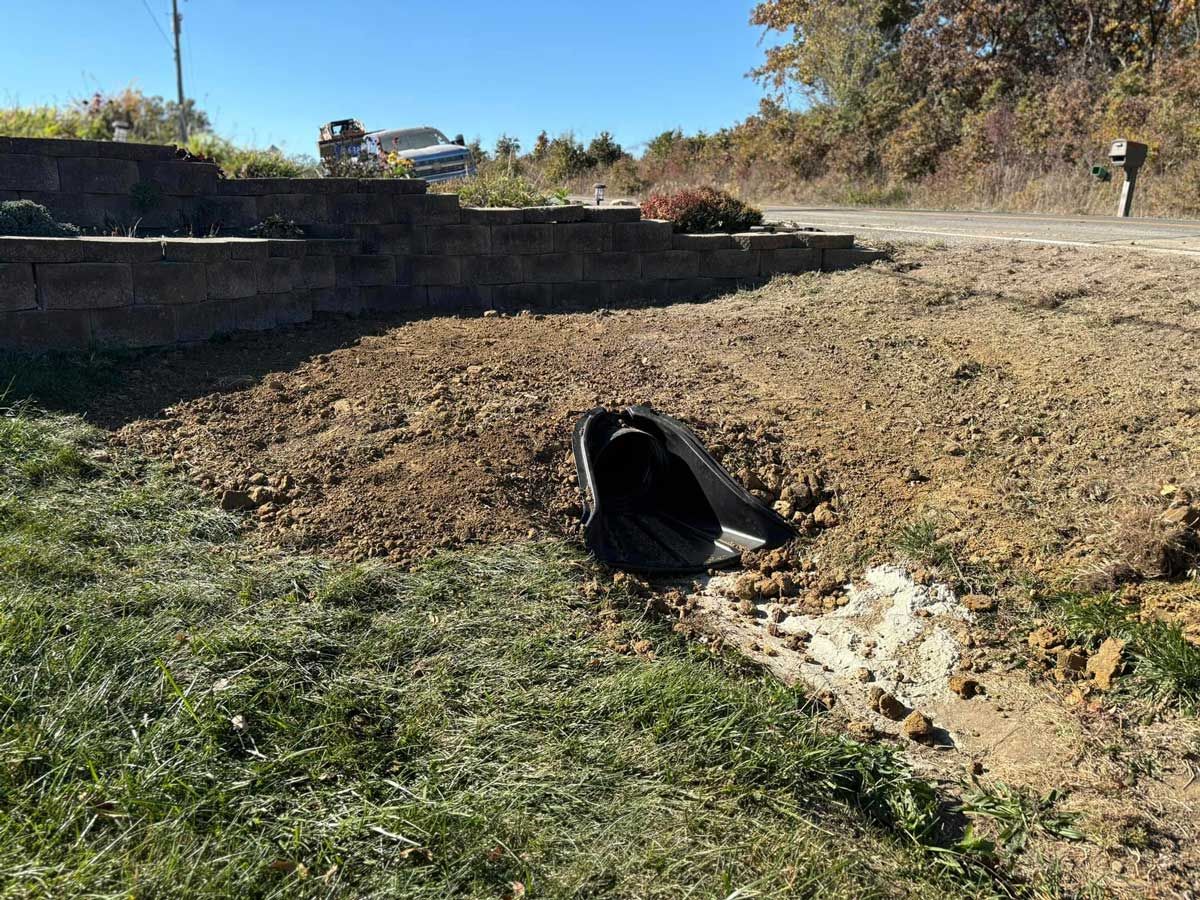 A black pipe is sitting in the middle of a dirt field next to a road.