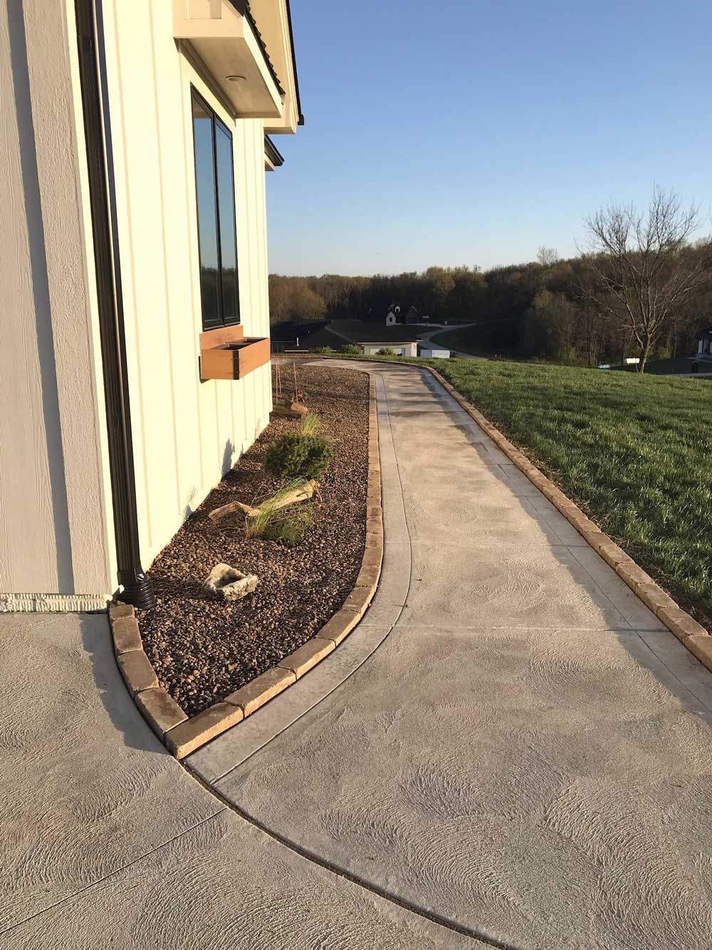 A concrete walkway leading to a house with a window.