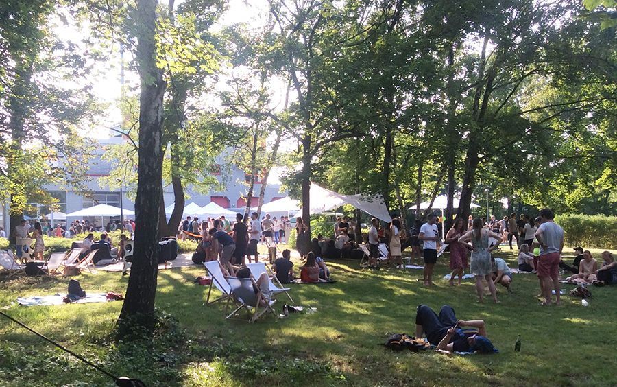 Im Park der Bridge Studios. Menschen in Liegestühlen, in Gruppen, lachend, unterhaltend. Hintergrund: Sonnensegel und Buffet