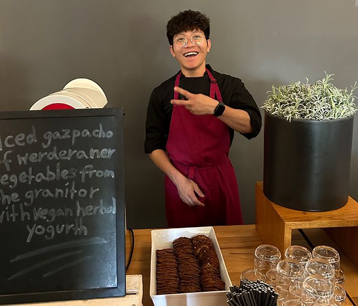 Junger Koch deutet lächelnd auf eine Speisentafel