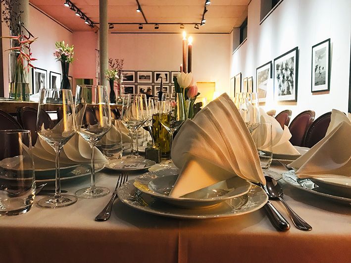 Dinner-Tisch. Vordergrund: Zur Bischofsmütze gefaltete Stoffserviette auf edlem Porzellanteller