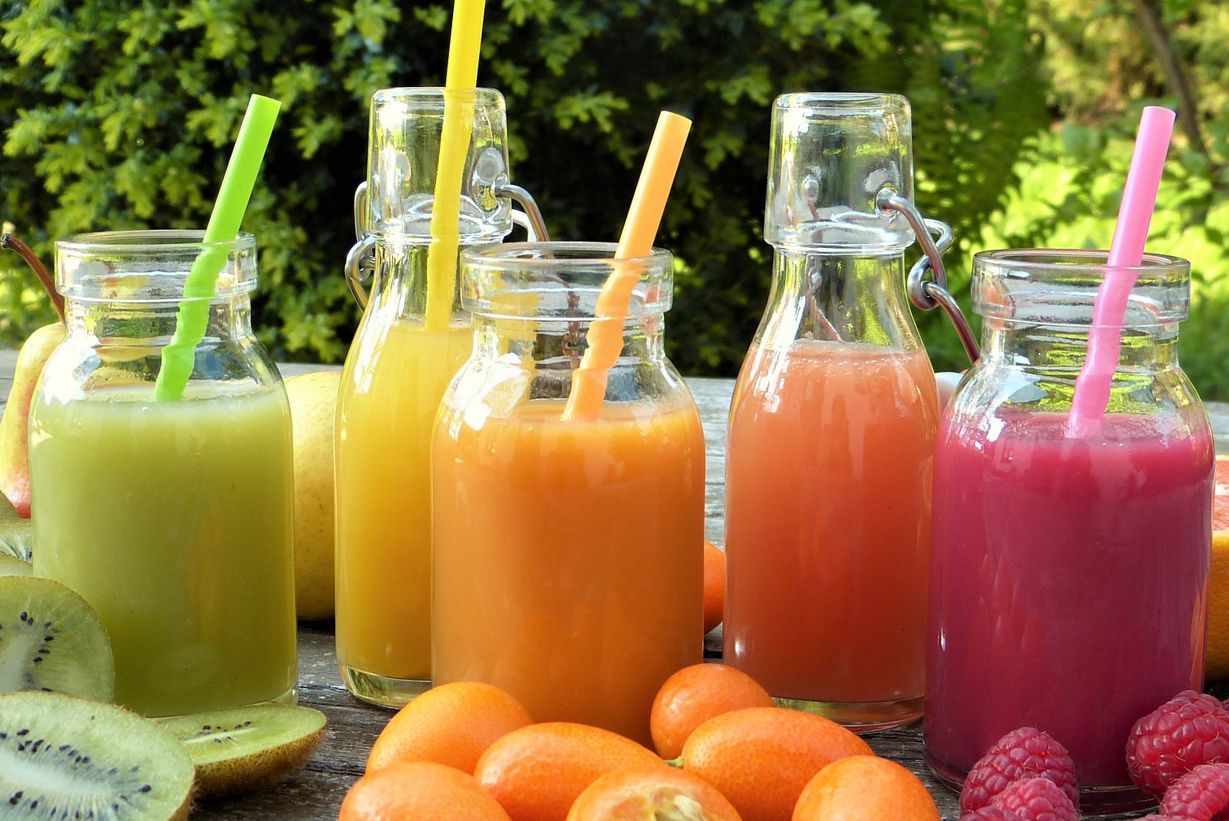 Bunter Fruchtsmoothies in verschiedenen Glasfläschen mit Trinkhalmen. Im Vordergrund frische Früchte