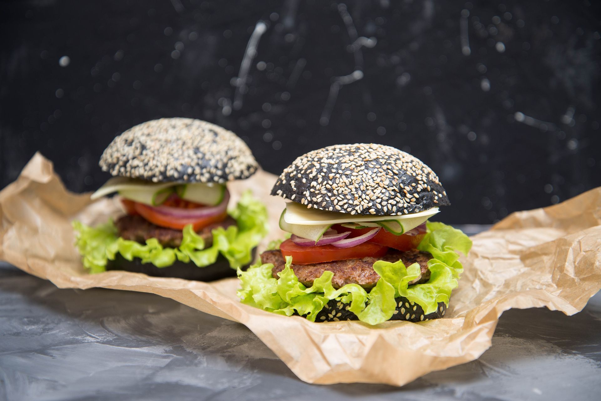 2 Burger in schwarzem Sesam-Brötchen. Darin Salat, Tomate, Burgerpattie. Serviert auf einer Papiertüte