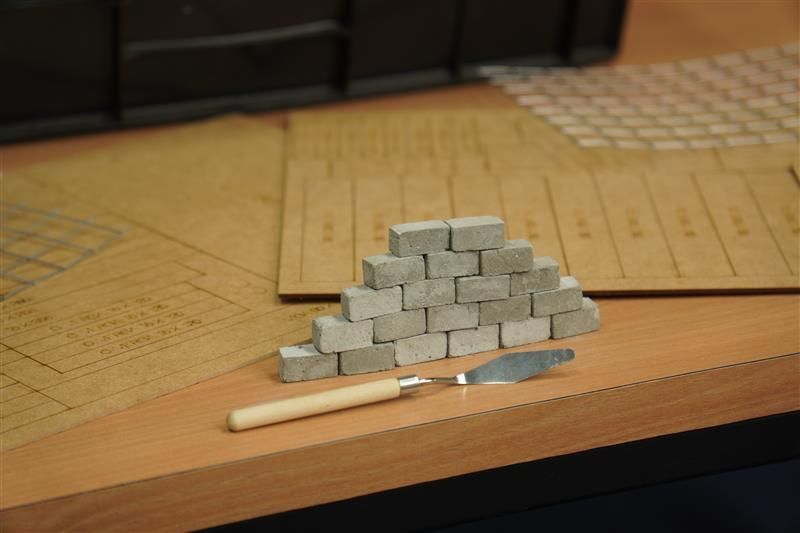 Miniature brick structure and trowel on a wooden table with construction documents.