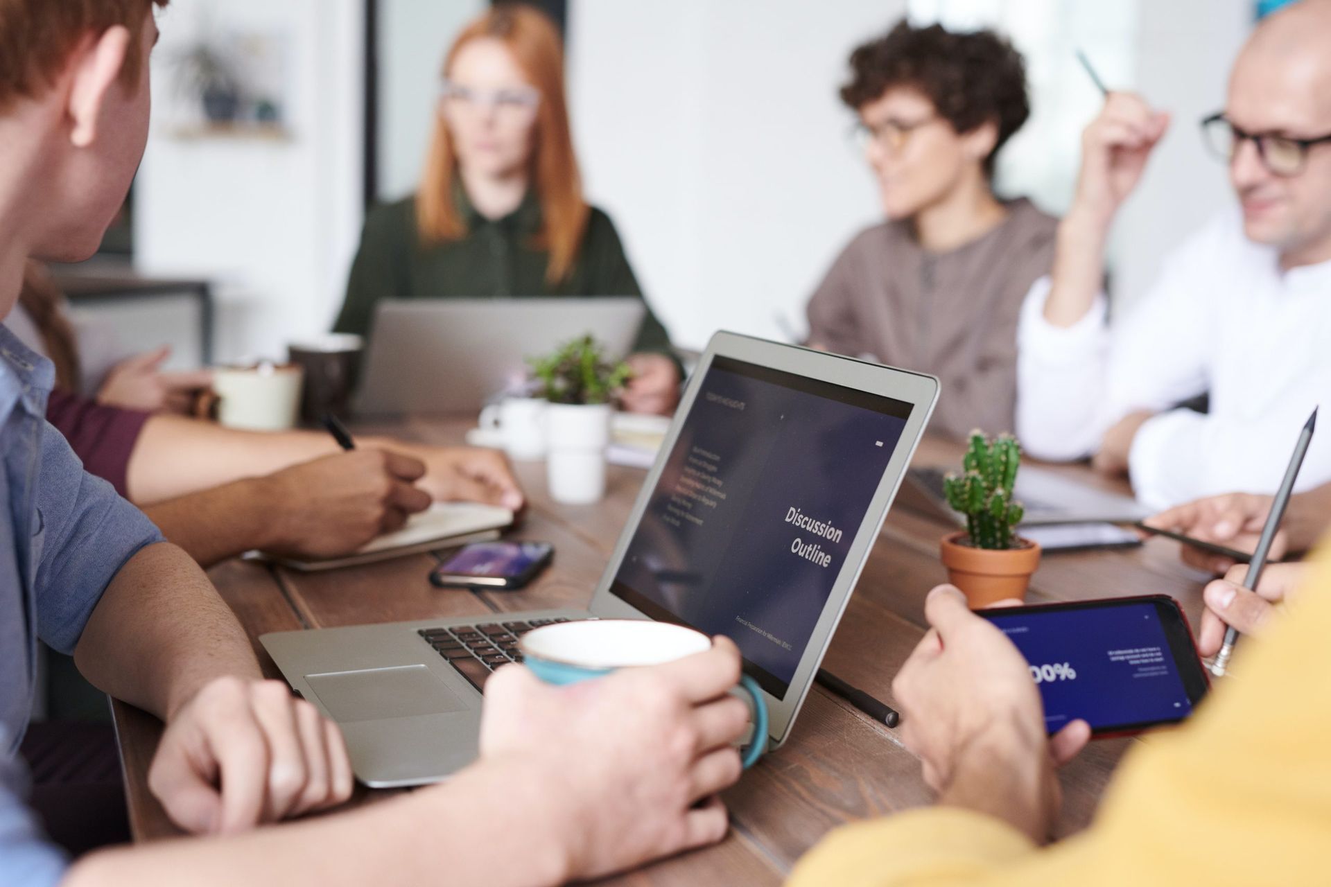 Pessoas em reunião de trabalho, com laptops, anotações e café sobre a mesa compartilhada.