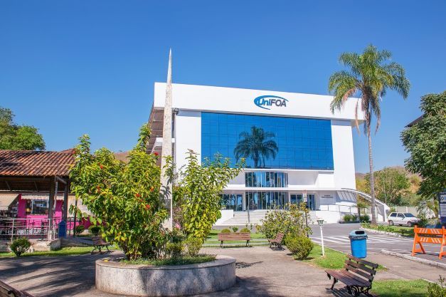 Fachada envidraçada do centro universitário UniFOA com jardins e bancos ao redor.