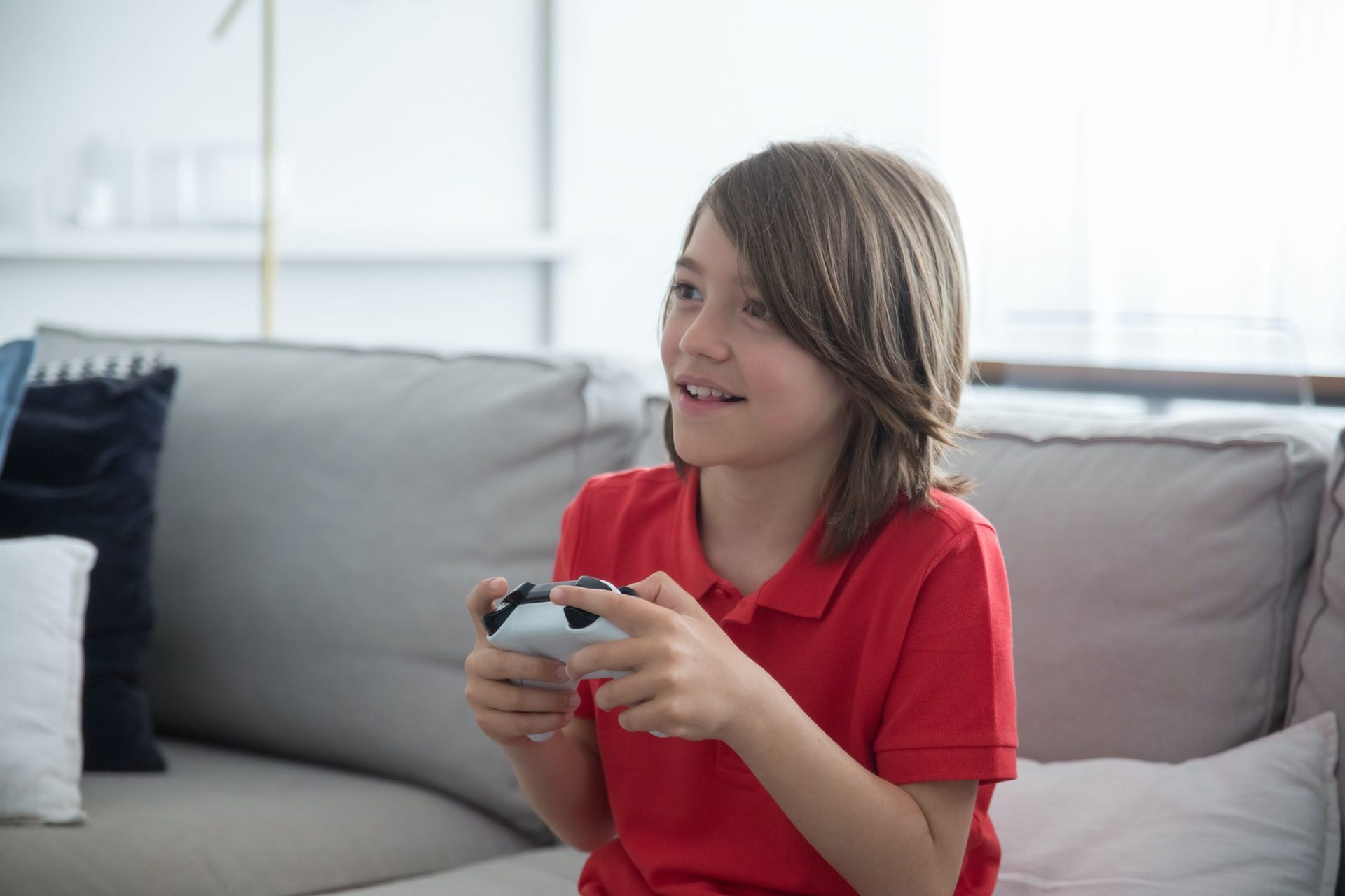 Criança sorridente jogando videogame sentada no sofá com controle nas mãos.