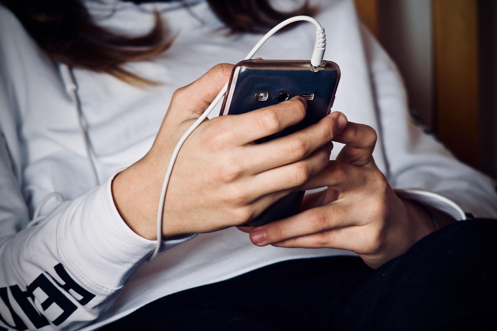 A woman in a white sweatshirt is using a cell phone