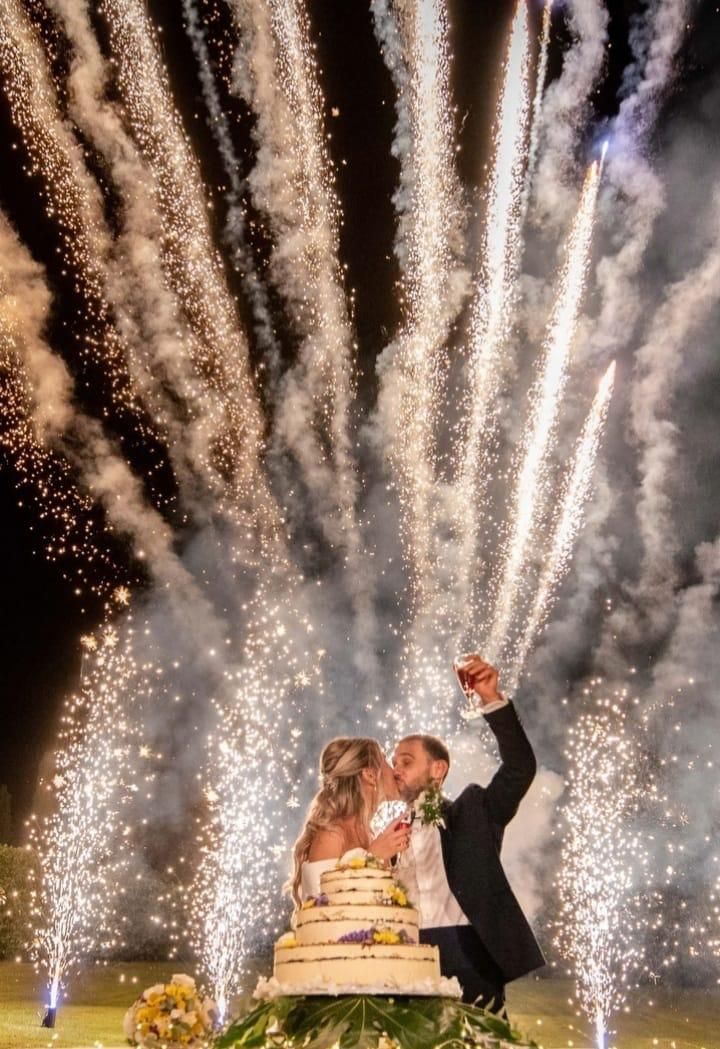 Una coppia si bacia vicino alla torta nuziale mentre i fuochi d'artificio esplodono sopra di loro.