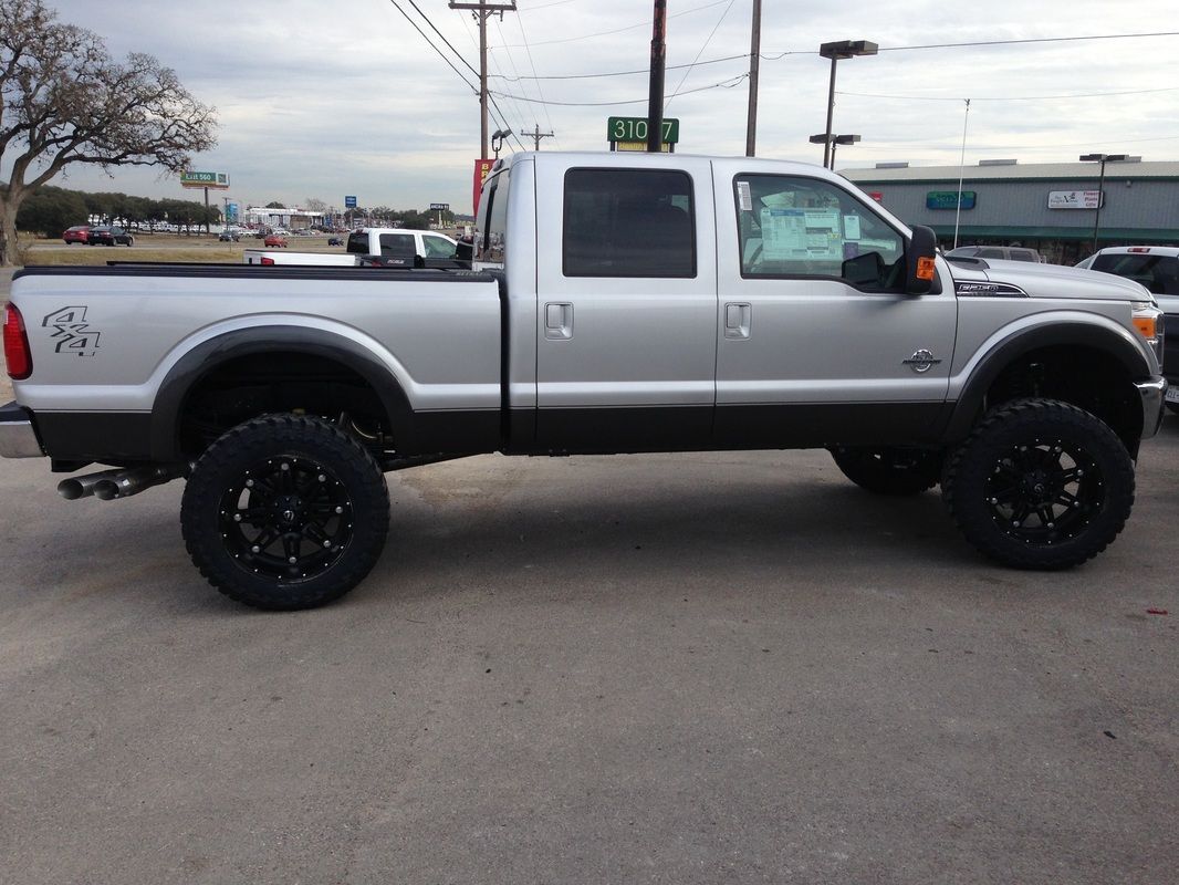 A silver truck with black wheels is parked in a parking lot