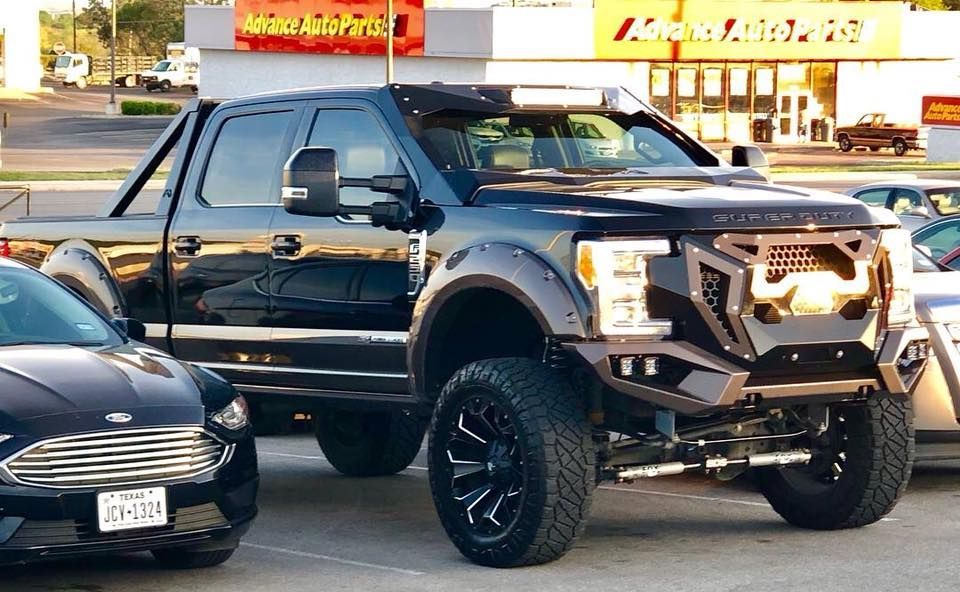 A black truck is parked next to a black car in a parking lot.