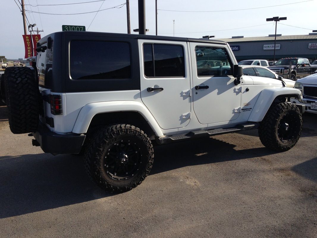 A white jeep with black wheels is parked in a parking lot