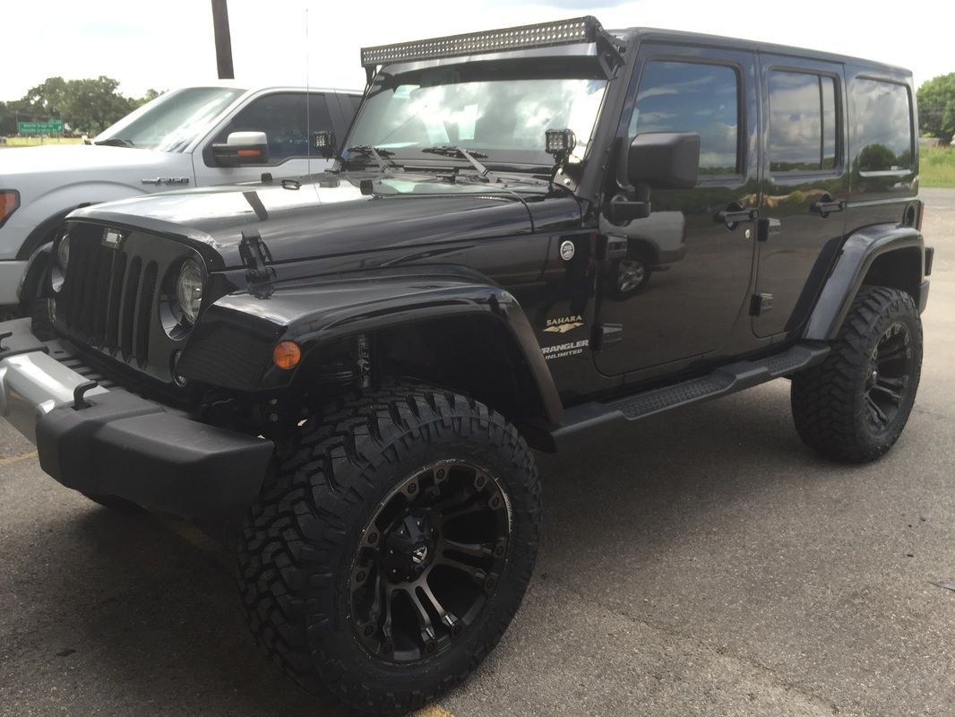 A black jeep is parked in a parking lot next to a white truck.