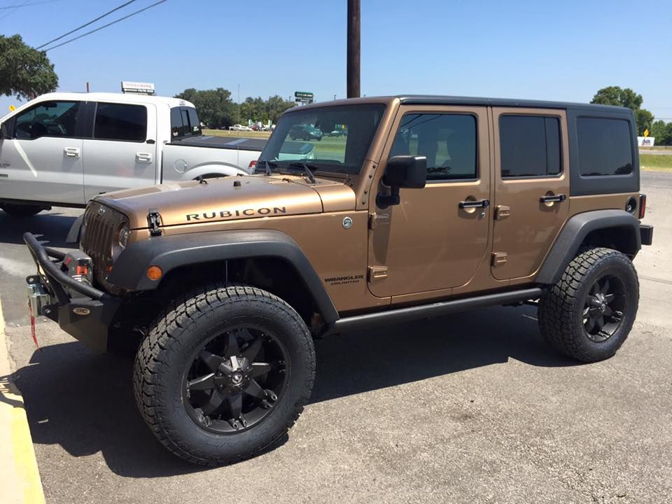 A brown jeep is parked in a parking lot next to a silver truck