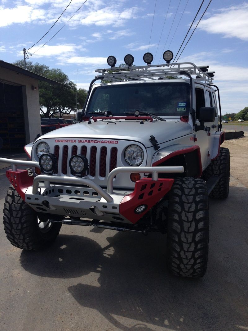 A white jeep with red trim is parked in front of a garage