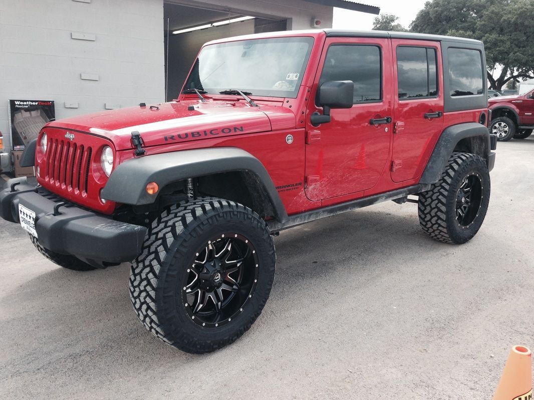 A red jeep with black wheels is parked in front of a garage.