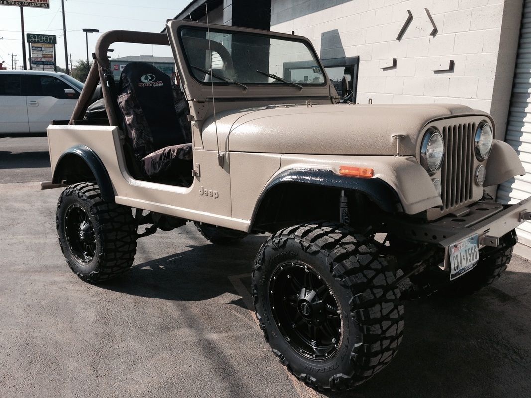 A tan jeep is parked in front of a building