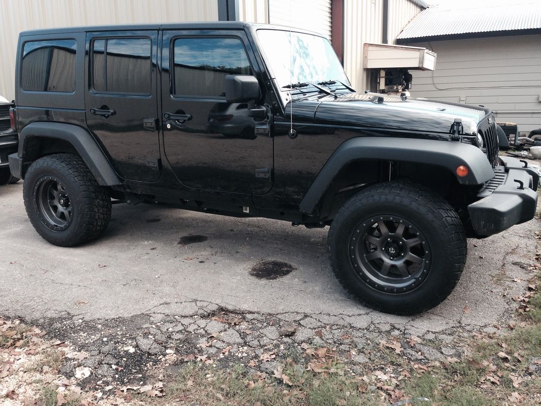 A black jeep is parked in a driveway in front of a building.