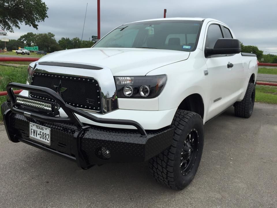 A white truck with a black bumper is parked on the side of the road