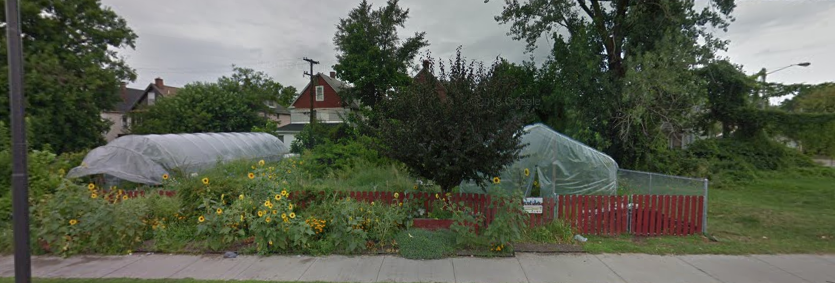Community garden with raised beds covered in tarp, a red fence, and a cloudy sky.