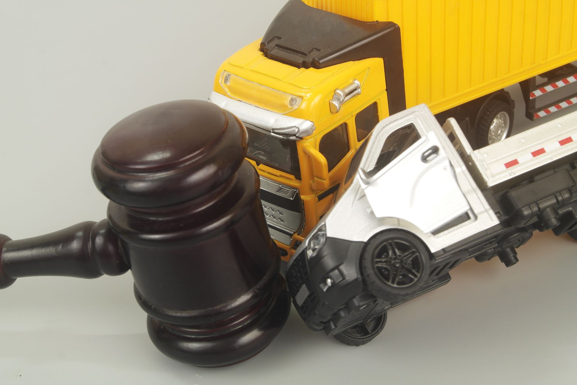 A judge's gavel and toy trucks on a grey background, representing truck accident attorney services. A judge's gavel and toy trucks on a grey background, representing truck accident attorney services.