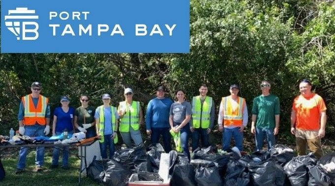 Port Tampa Bay volunteers stand in front of a line of collected trash bags after a community cleanup event.