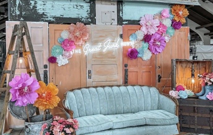 Colorful floral backdrop with vintage doors, sofa, and ladder, for an event. Neon sign says “Our Great Journey.” Colorful floral backdrop with vintage doors, sofa, and ladder, for an event. Neon sign says “Our Great Journey.”