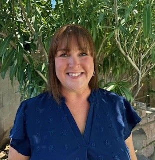 A woman in a blue shirt is smiling in front of a tree.