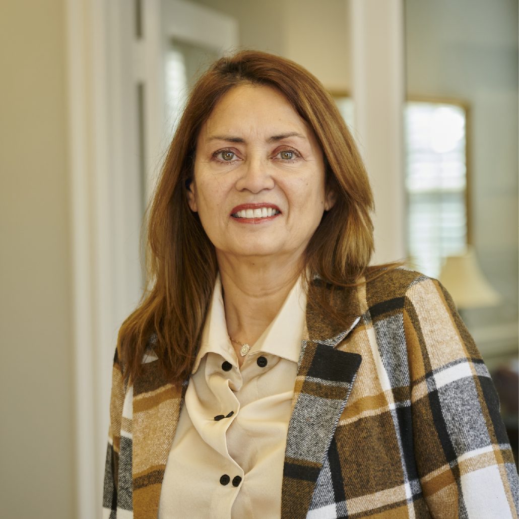 A woman wearing a plaid jacket and a white shirt is smiling for the camera.