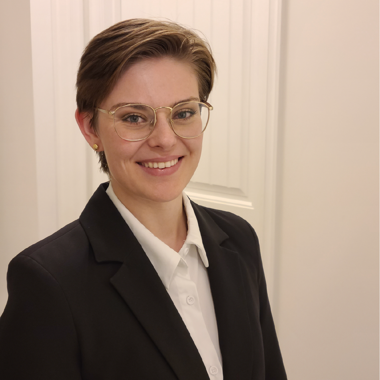 A woman wearing glasses and a suit is smiling for the camera