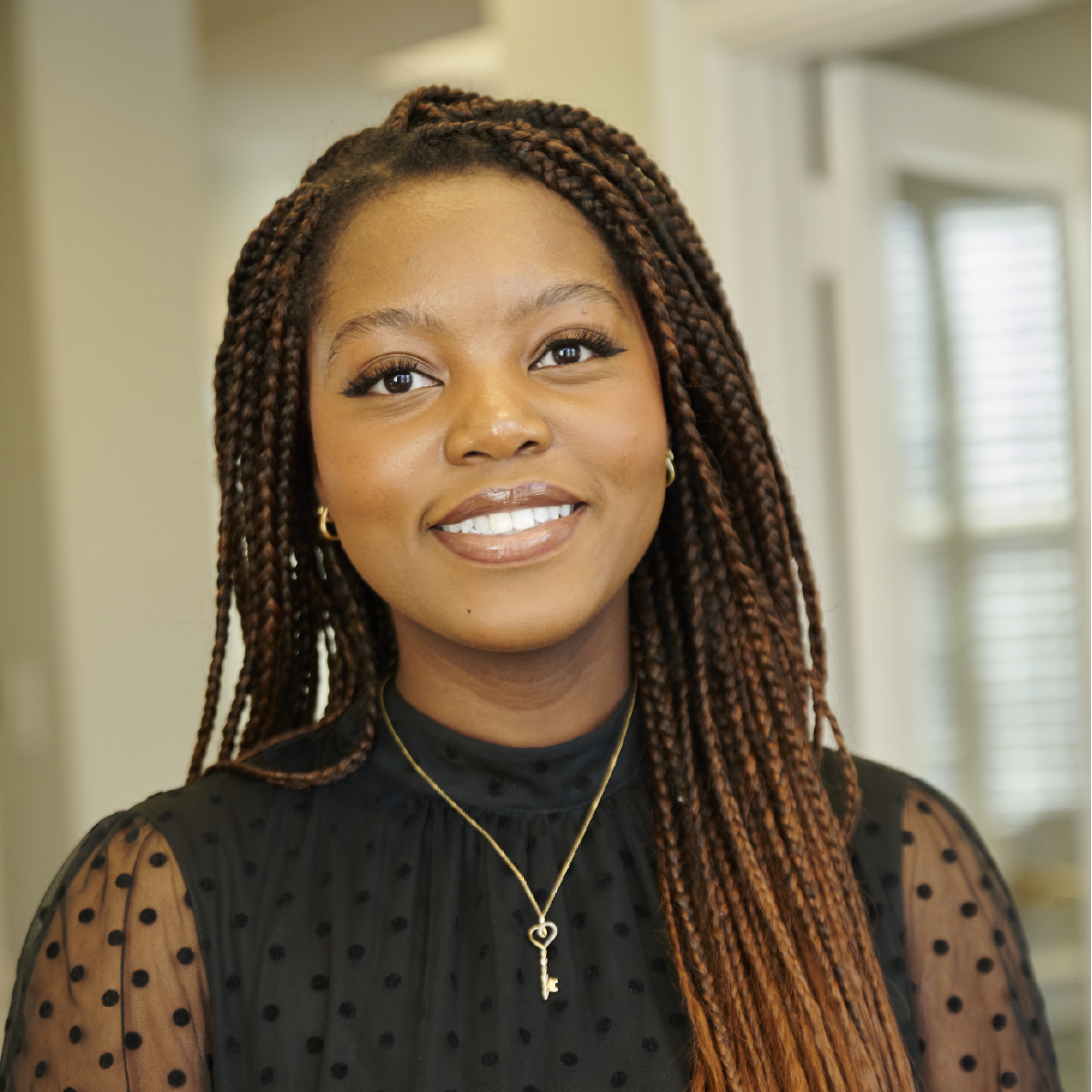 A woman with braids is smiling and wearing a necklace with a key pendant