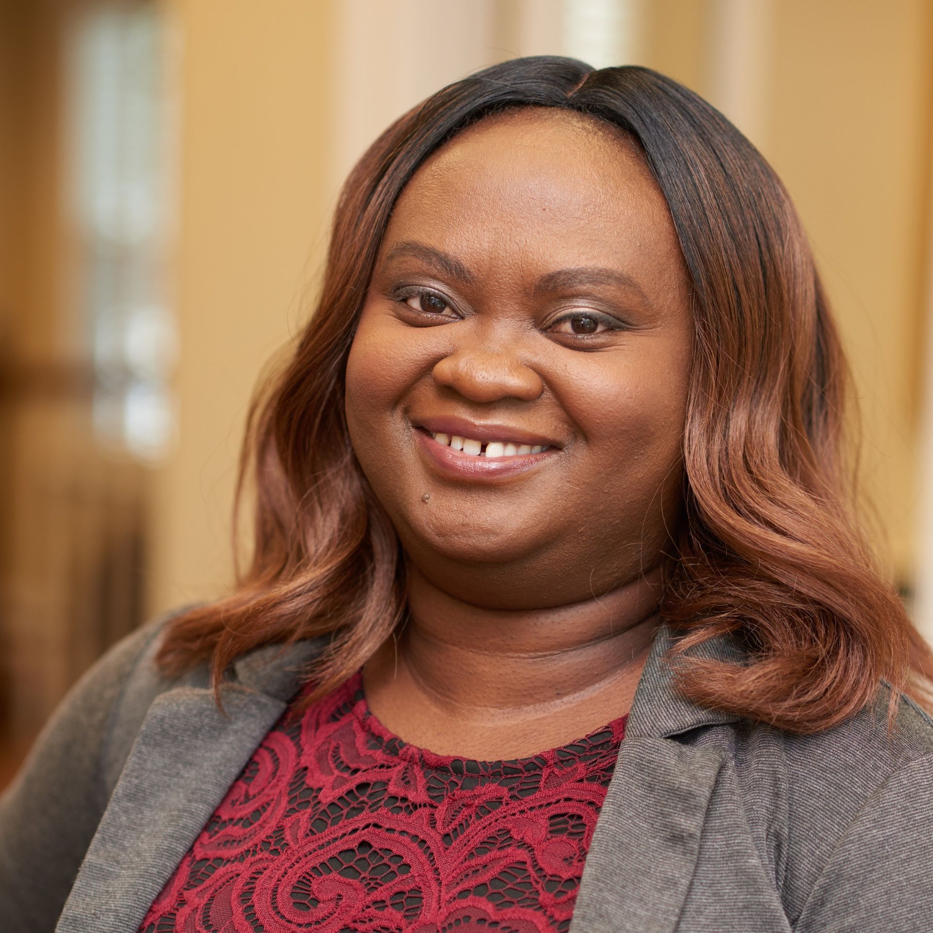 A woman in a red top and gray jacket is smiling for the camera.