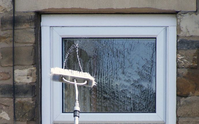Window cleaning brush on pole spays water onto glass