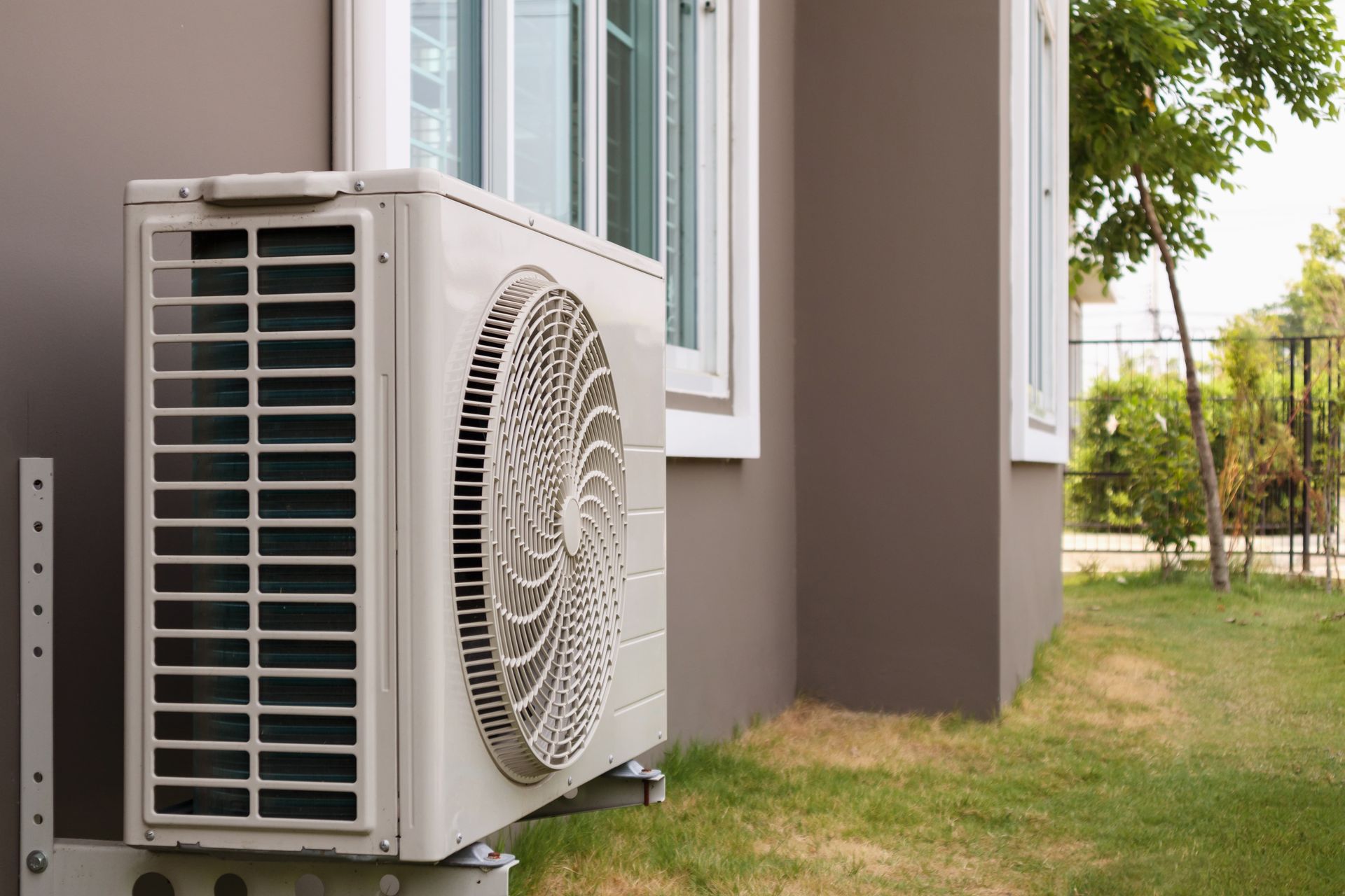 A white air conditioner is sitting on the side of a house next to a window.