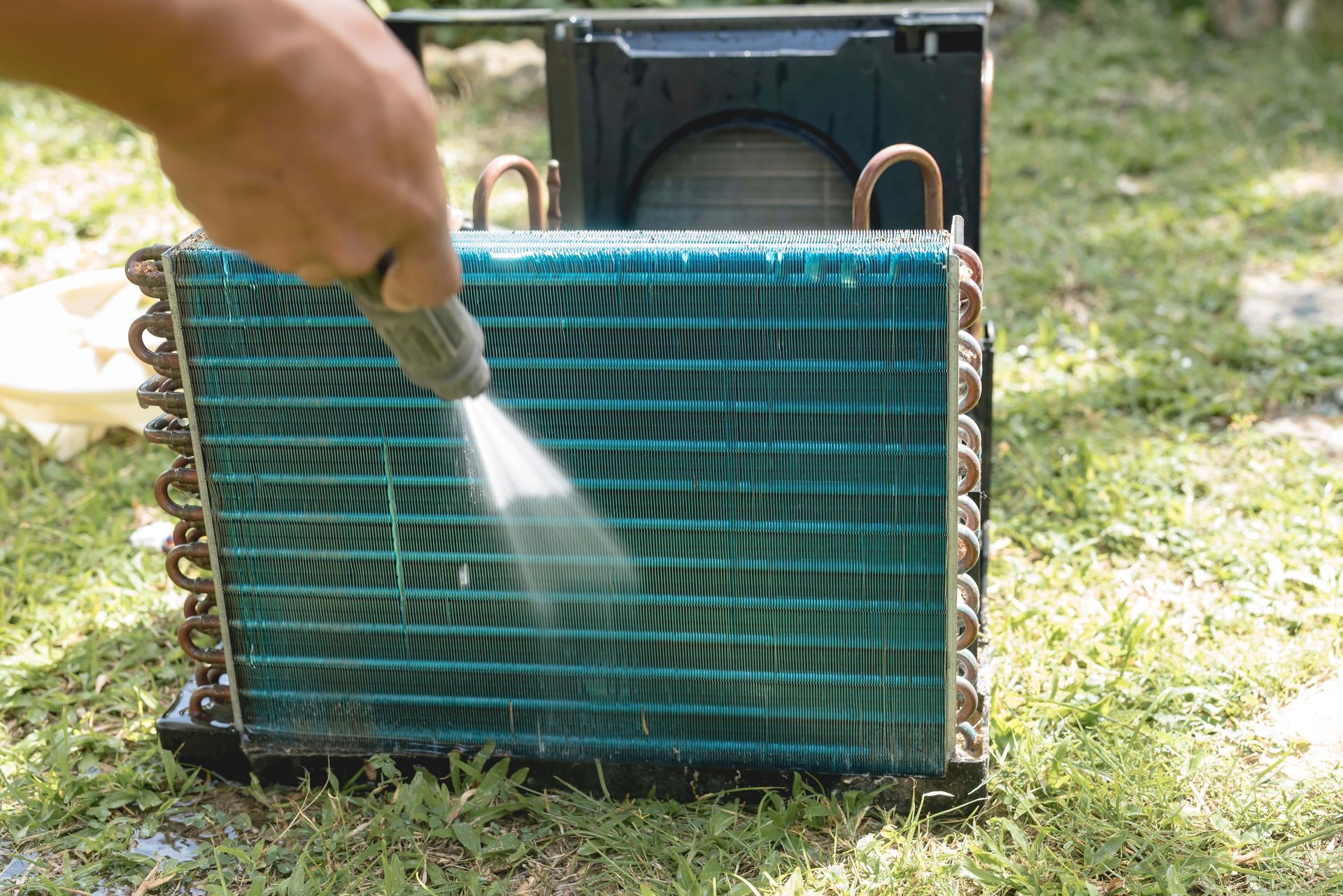 A person is cleaning an air conditioner coil with a spray bottle.