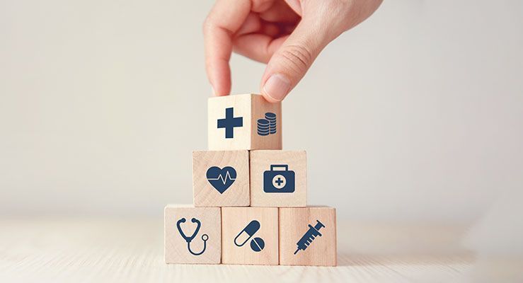 A hand is stacking wooden blocks with medical icons on them.