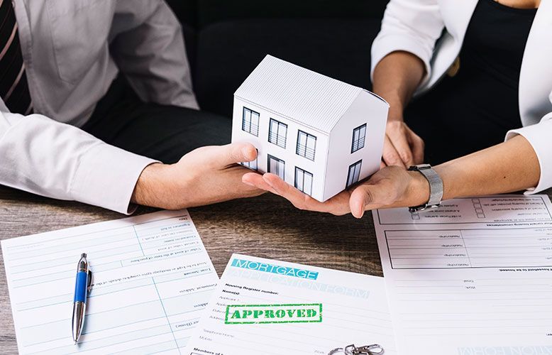 A man and a woman are holding a model house in their hands.