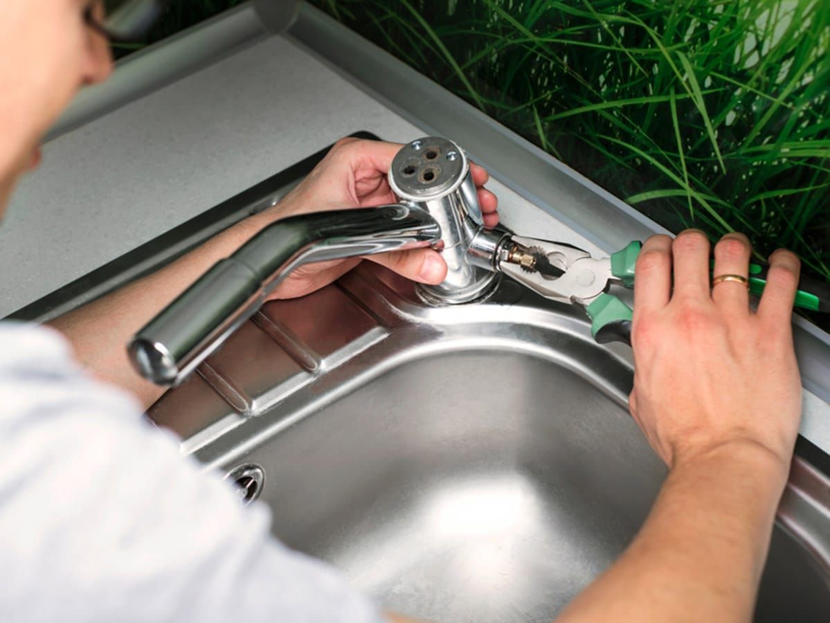 Person Using Pliers to Work on a Faucet in a Kitchen Sink — Expert Plumbing & Solar Services Bathurst in Kelso, NSW
