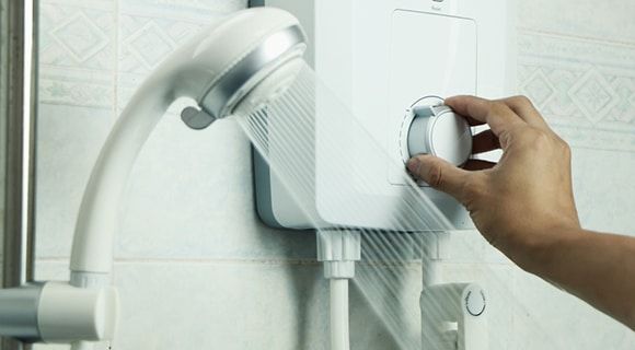 Hand Adjusting the Temperature Dial on a White Electric Shower Unit — Expert Plumbing & Solar Services Bathurst in Kelso, NSW