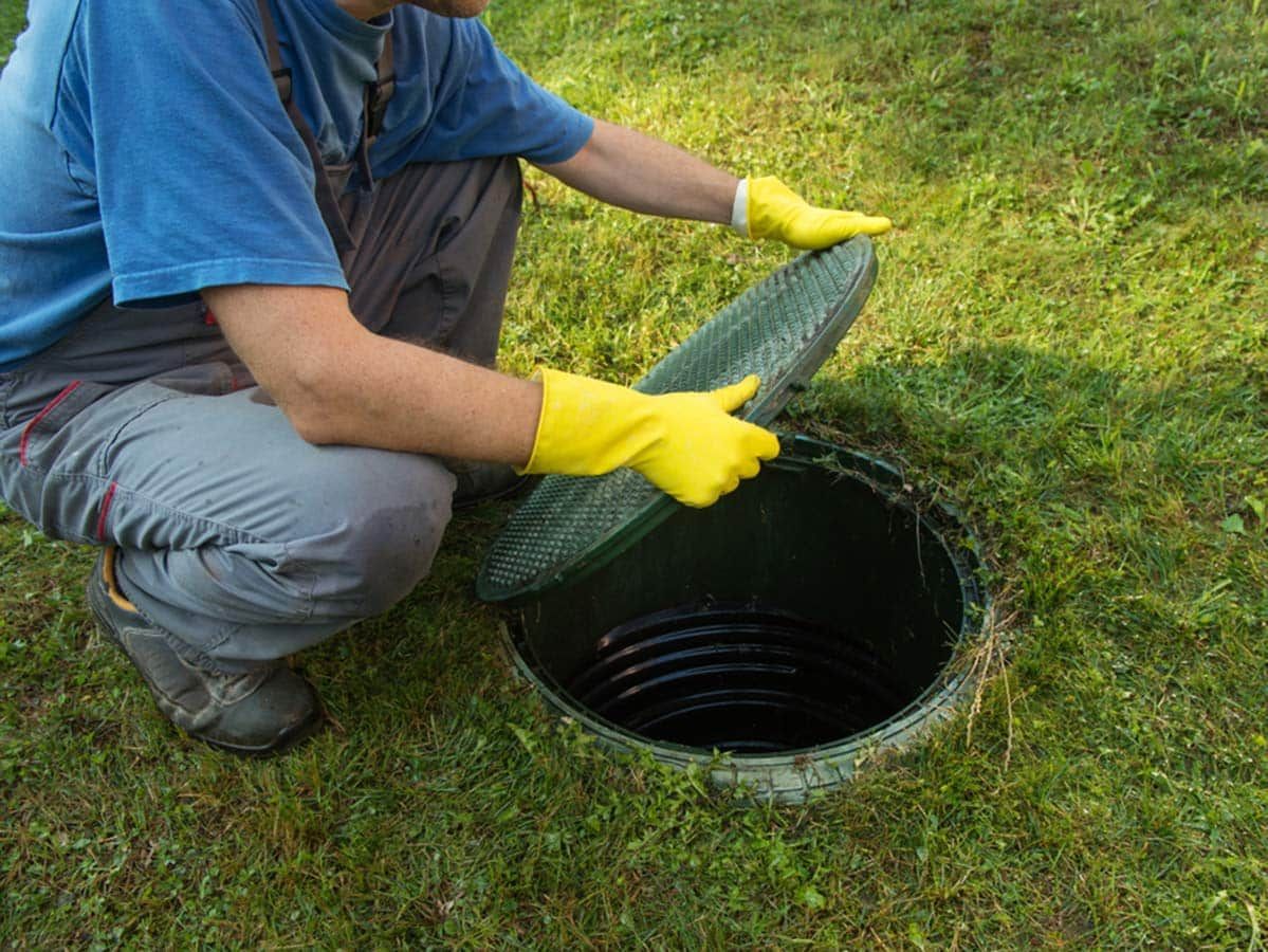 Person in Overalls and Gloves Opening a Septic Tank in Grassy Yard — Expert Plumbing & Solar Services Bathurst in Lithgow, NSW