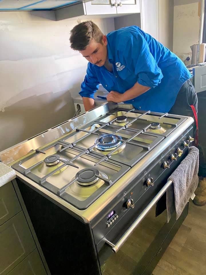 Person Installing a Gas Cooktop in a Kitchen — Expert Plumbing & Solar Services Bathurst in Kelso, NSW