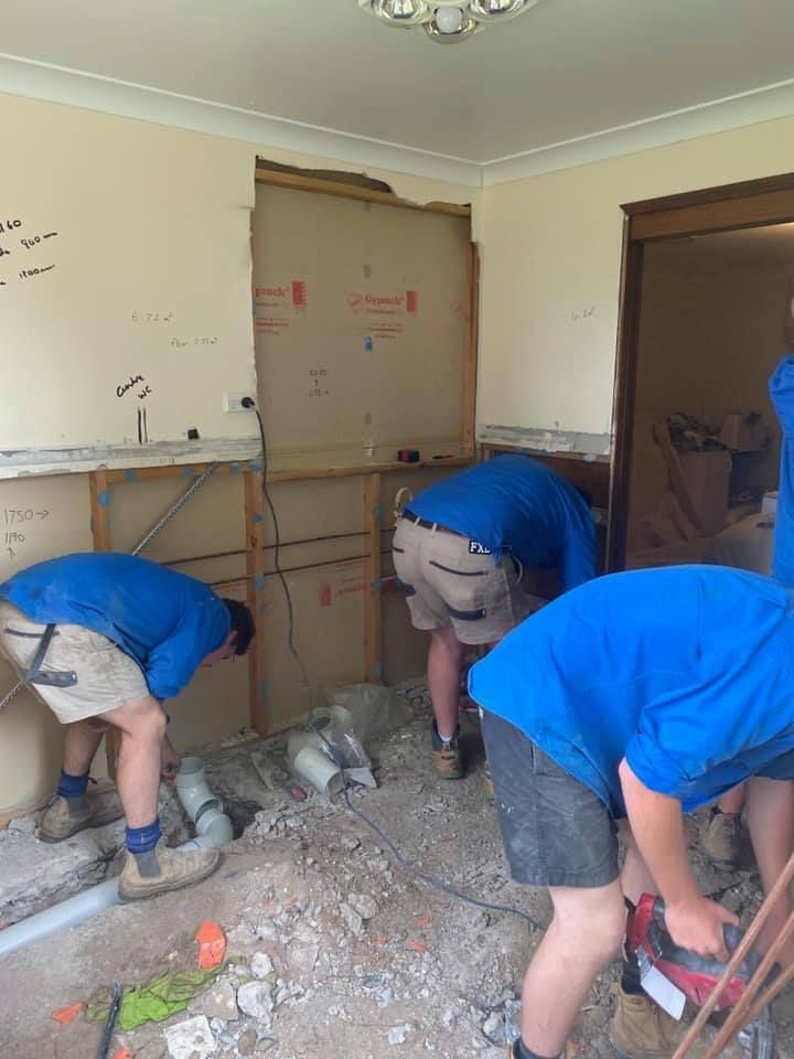 Workers in Blue Shirts Demolish a Wall in a Room — Expert Plumbing & Solar Services Bathurst in Kelso, NSW