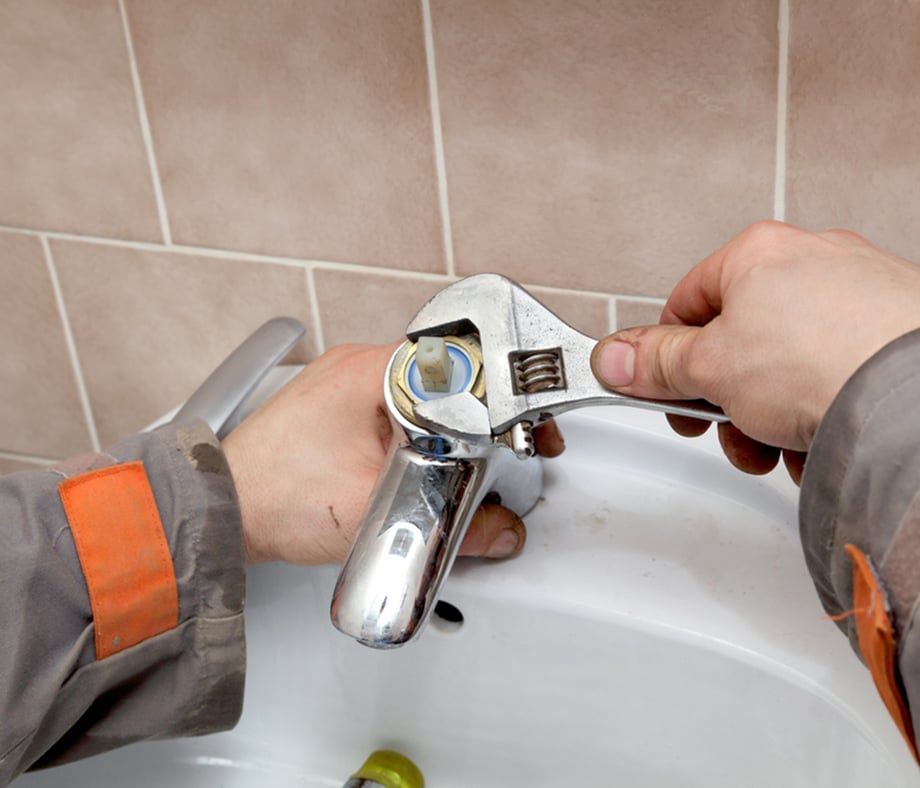 Person Using Adjustable Wrench on Bathroom Faucet in a White Sink — Expert Plumbing & Solar Services Bathurst in Kelso, NSW