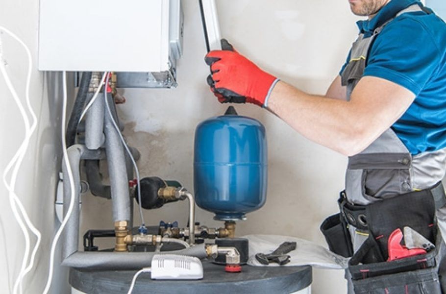 Plumber in Blue Shirt and Gray Overalls Working on a Boiler — Expert Plumbing & Solar Services Bathurst in Kelso, NSW