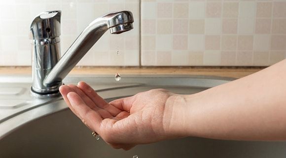a Person's Hand Under a Dripping Faucet in a Stainless Steel Sink — Expert Plumbing & Solar Services Bathurst in Kelso, NSW