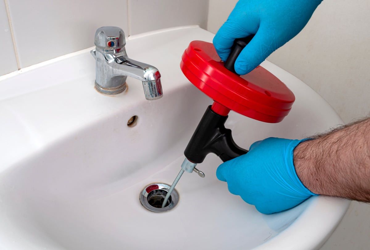 Hands in Blue Gloves Using a Drain Snake on a White Bathroom Sink — Expert Plumbing & Solar Services Bathurst in Lithgow, NSW