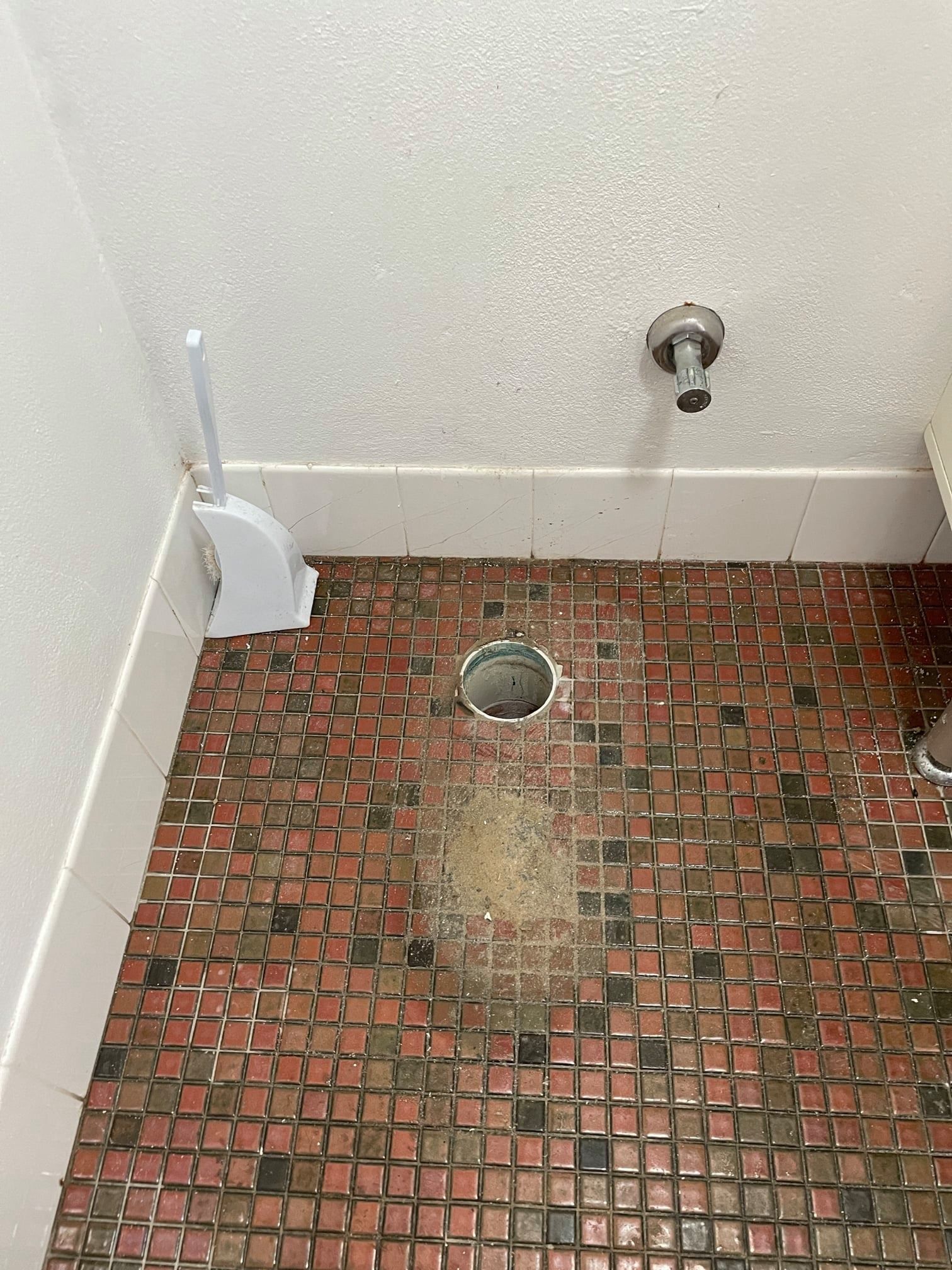 Toilet Drain Hole in Bathroom Floor. Red and Black Tiled Floor, White Walls — Expert Plumbing & Solar Services Bathurst in Kelso, NSW