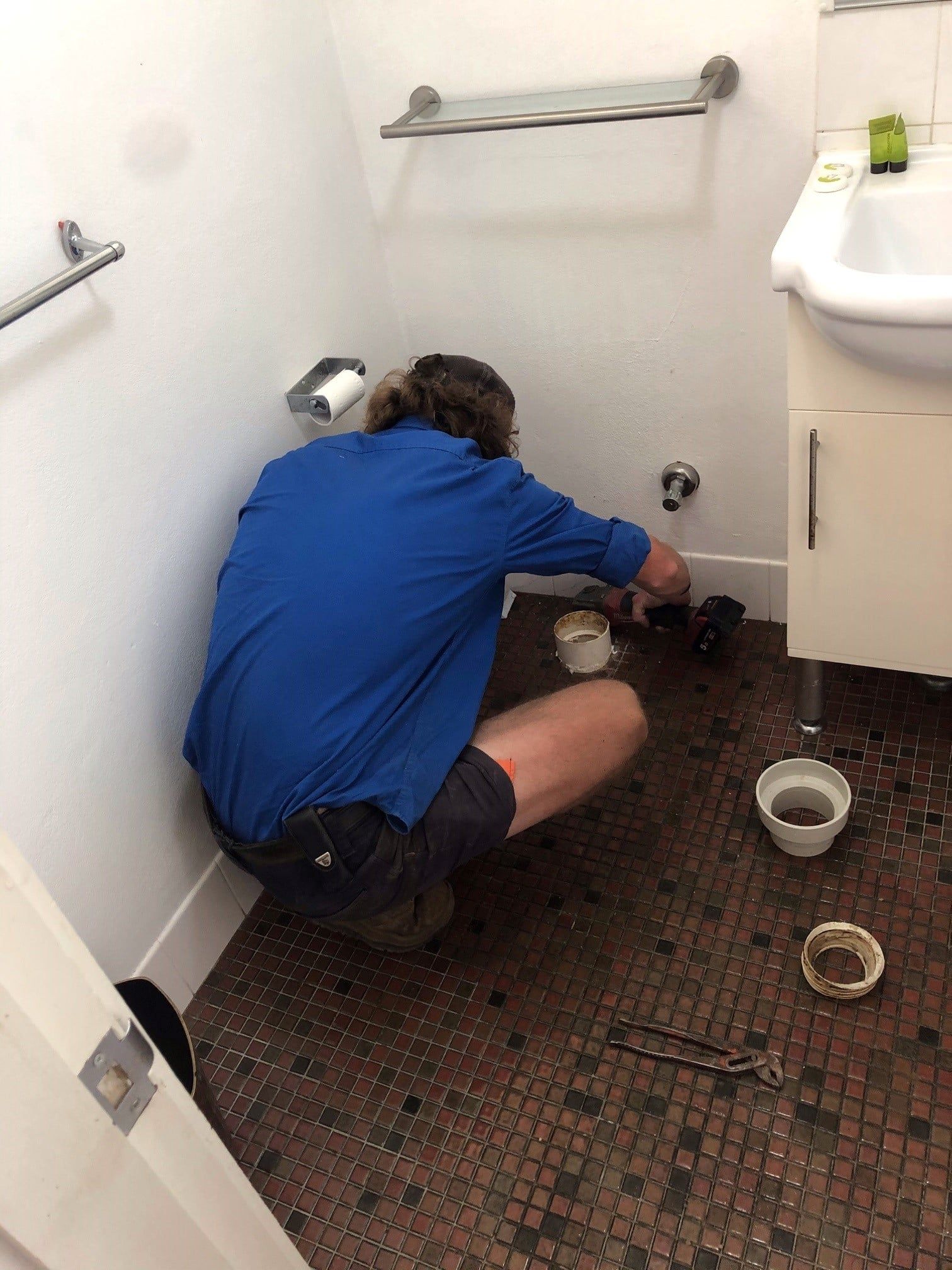 Man in Blue Shirt Working on Plumbing in a Bathroom